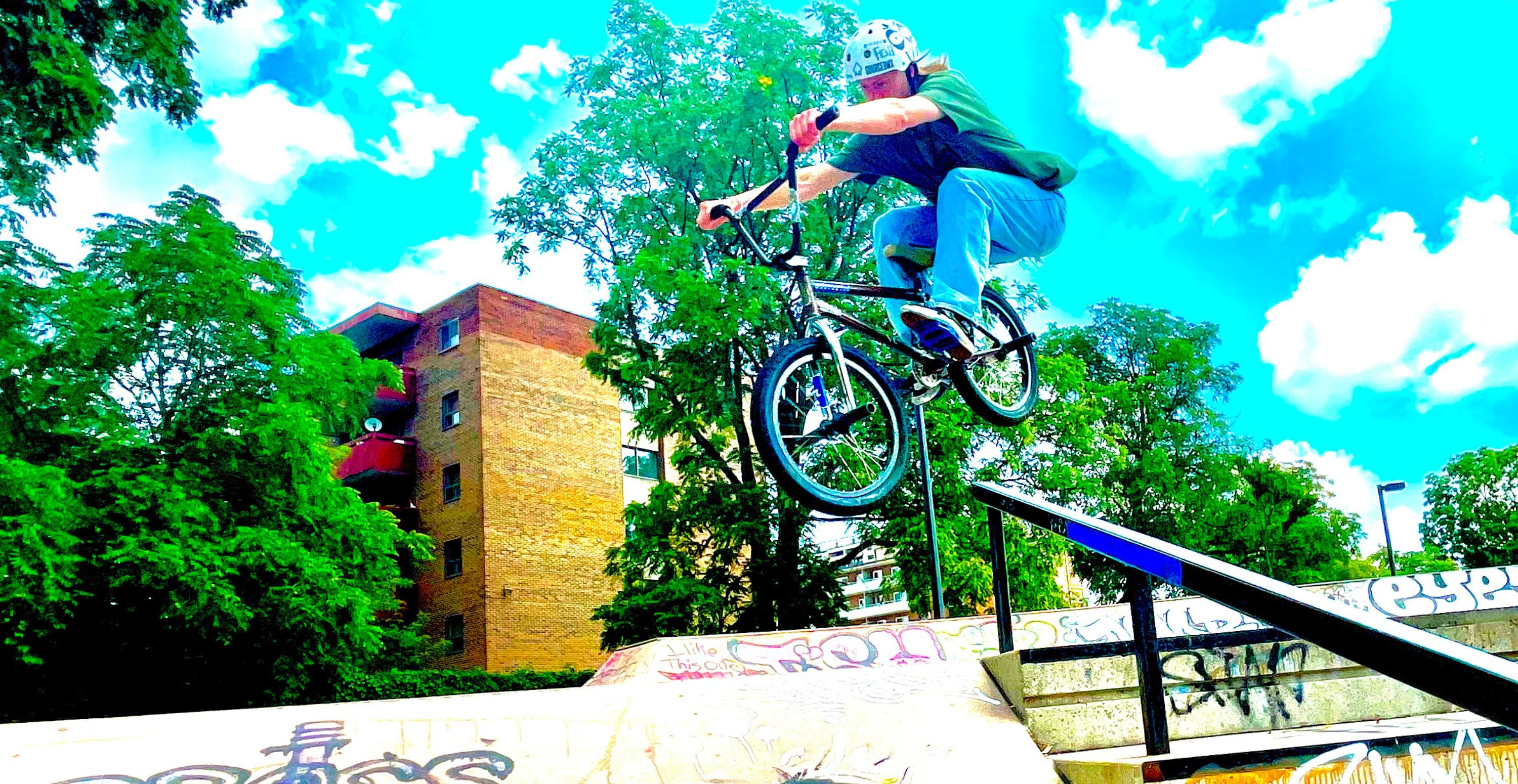 young man wearing t-shirt and jeans riding bmx at urban skate park